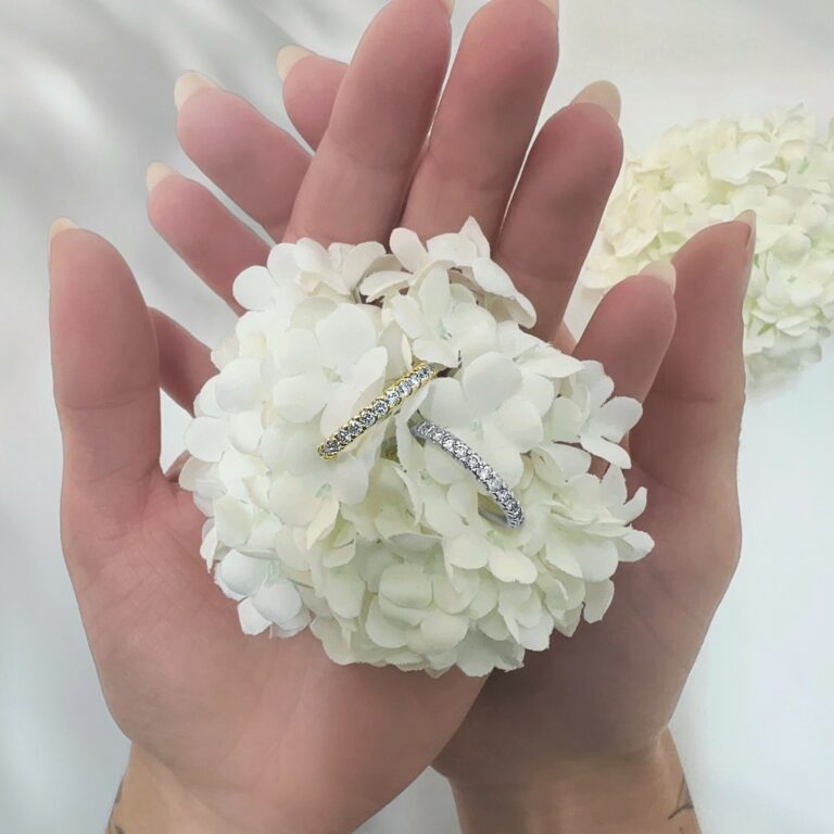 Zwei funkelnde, pavébesetzte Ringe – einer in Gelbgold, einer in Weißgold – liegen auf einem weißen Hortensienbüschel, gehalten in zwei Händen.